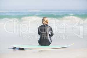Rear view of woman in wetsuit sitting with surfboard on the beac