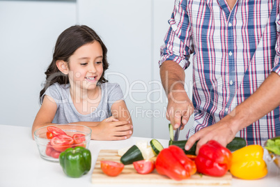 Midsection of father cutting vegetables with daughter