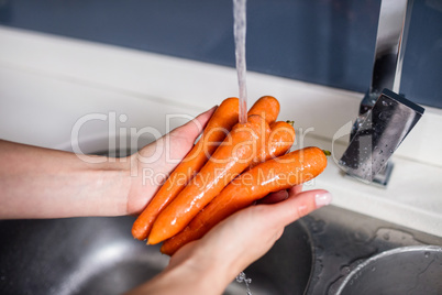 Woman washing carrots at kitchen washbasin