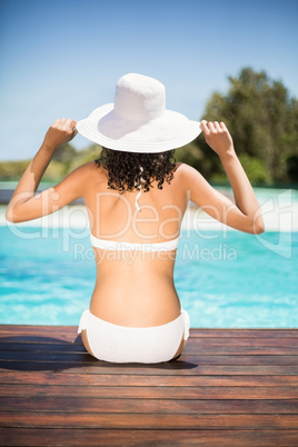 Rear view of woman wearing white bikini and hat sitting near poo