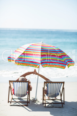 Cute mature couple doing high five on deckchairs