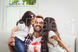Father holding gift box and daughters kissing him