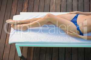 Beautiful woman in blue bikini lying on sun lounger by poolside