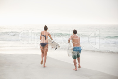 Rear view of couple running with a surfboard on the beach