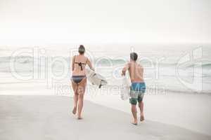 Rear view of couple running with a surfboard on the beach