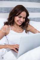 Woman smiling while using laptop on bed