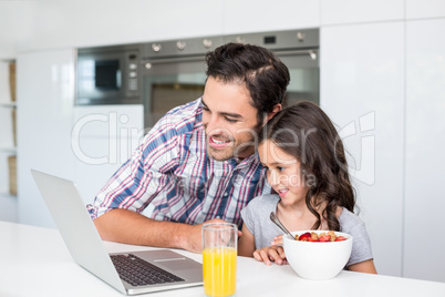 Smiling father and daughter using laptop with breakfast on table