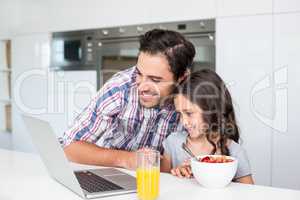 Smiling father and daughter using laptop with breakfast on table