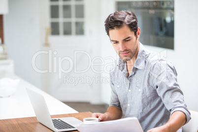 Young man reading documents while sitting at desk with laptop