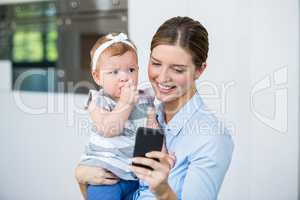 Woman using mobile phone while carrying baby girl