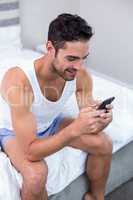 Man using mobile phone while sitting on bed