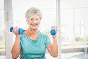 Portrait of smiling senior woman holding dumbbell