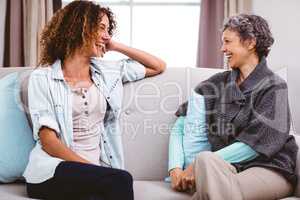 Mother and daughter laughing while sitting on sofa