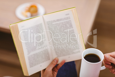 Midsection of woman reading book while holding coffee cup