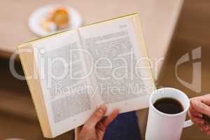 Midsection of woman reading book while holding coffee cup