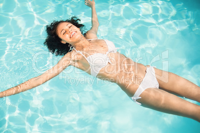 Beautiful woman in white bikini floating in swimming pool