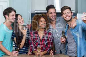 Multi-ethnic friends with alcohol taking selfie in kitchen