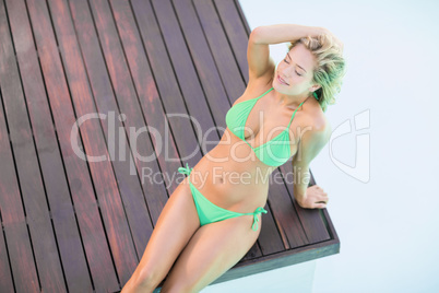 Beautiful woman in green bikini relaxing by pool side