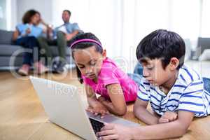 Brother and sister lying on floor and using laptop