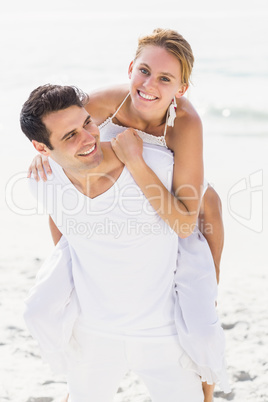 Man giving a piggy back to woman on the beach