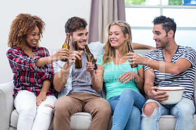 Multi-ethnic friends toasting beer while sitting on sofa