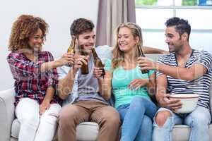 Multi-ethnic friends toasting beer while sitting on sofa