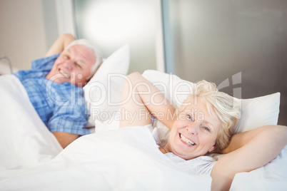 Portrait of happy senior woman relaxing besides man on bed