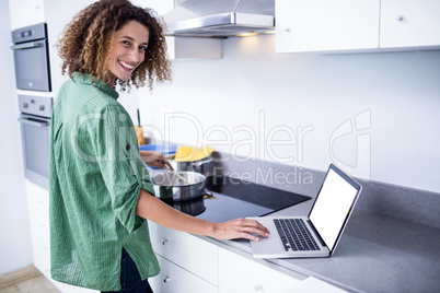 Portrait of woman working on laptop while cooking