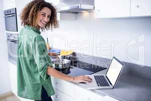 Portrait of woman working on laptop while cooking