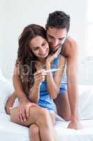 Young woman holding pregnancy test while husband embracing on be