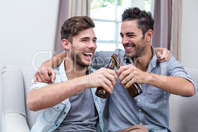 Cheerful young male friends toasting beer at home