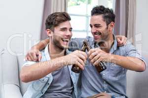 Cheerful young male friends toasting beer at home