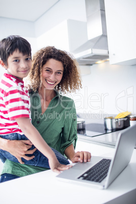 Mother using laptop with son in kitchen