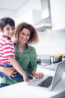 Mother using laptop with son in kitchen