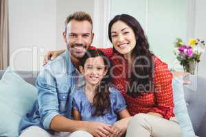 Happy parents sitting with daughter on sofa