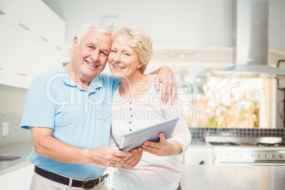 Portrait of happy senior couple holding digital tablet in kitche