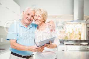 Portrait of happy senior couple holding digital tablet in kitche