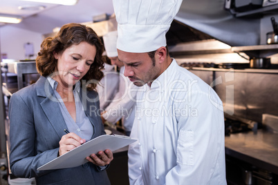 Female restaurant manager writing on clipboard while interacting