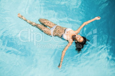 Beautiful woman in white bikini floating in swimming pool