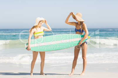 Two women holding a surfboard on the beach