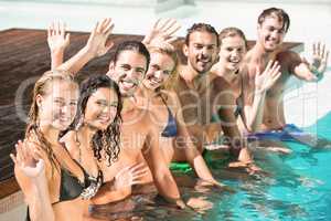 Portrait of friends waving hands in swimming pool