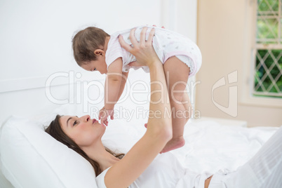 Mother carrying baby girl while lying on bed