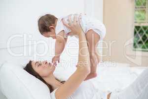 Mother carrying baby girl while lying on bed