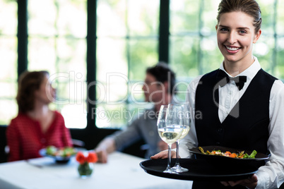 Waitress holding meal and wine glasses in restaurant