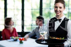 Waitress holding meal and wine glasses in restaurant