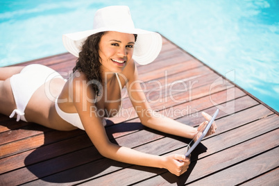 Woman in hat and bikini using digital tablet on wooden decker by