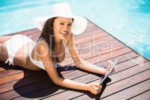 Woman in hat and bikini using digital tablet on wooden decker by