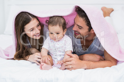 Couple enjoying with baby under blanket on bed