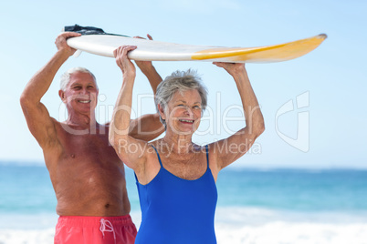 Cute mature couple holding a surfboard over their heads