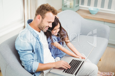 Smiling father and daughter using laptop while sitting on sofa